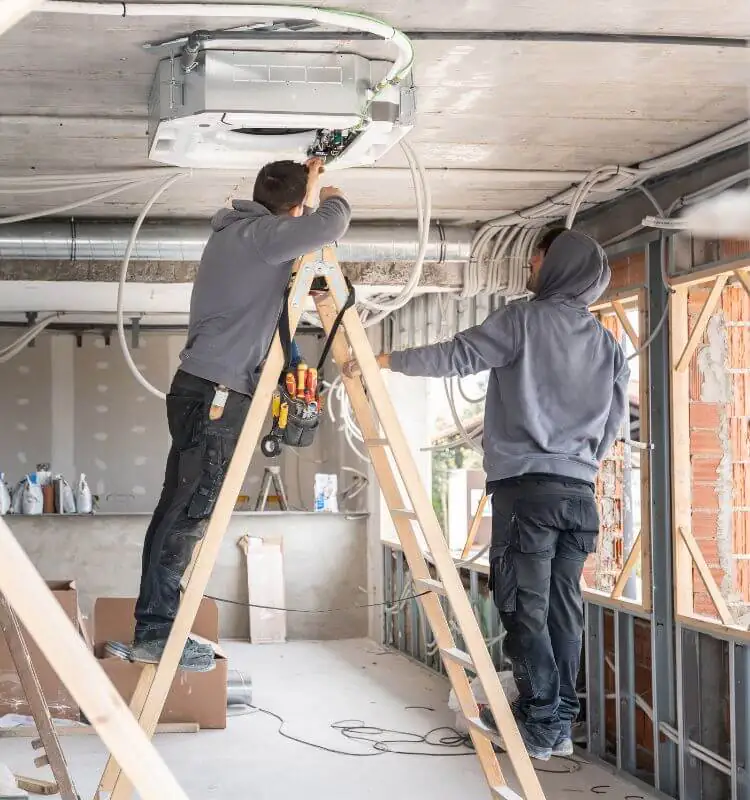 Two engineers on ladders fitting air conditioning pipework in a commercial unit in Bristol
